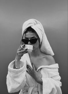 a woman in a bathrobe drinking from a cup while wrapped in a towel