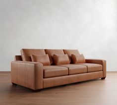 a brown leather couch sitting on top of a hard wood floor next to a white wall