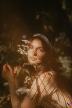 a woman holding flowers in her hands and looking up at the sun shining on her face