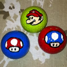 three different colored balls with mario and luigi faces painted on them, sitting on a surface