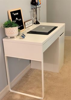 a laptop computer sitting on top of a white desk next to a potted plant