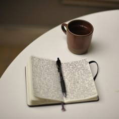 an open book with a pen sitting on top of it next to a coffee cup