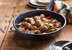 a bowl filled with meat and vegetables on top of a wooden table next to plates