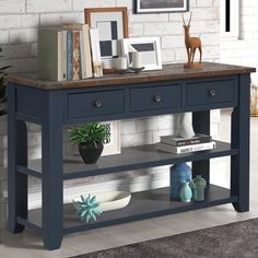 a blue table with two drawers and some pictures on it's shelf next to a potted plant