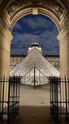 the pyramid is lit up at night in front of an ornate gated area with wrought iron railings