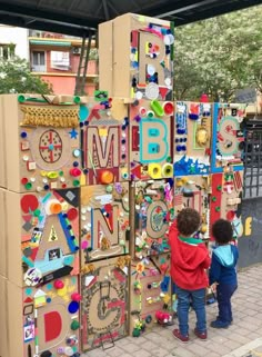 two children are standing in front of a cardboard structure with letters and numbers on it