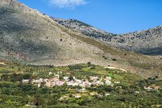 a small village nestled on the side of a large hill in front of some mountains