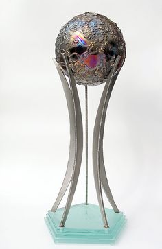 a metal sculpture with two curved legs and a colorful object in the middle on a blue base