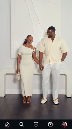 a man and woman standing next to each other in front of a white wall holding hands