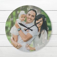 a man and woman holding a baby in front of a white wall clock with black hands