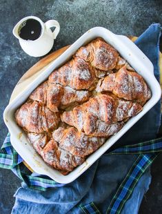 a baking dish filled with cinnamon rolls next to a cup of coffee on a blue towel