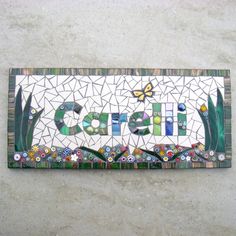 a mosaic name sign on the side of a building with flowers and butterflies around it