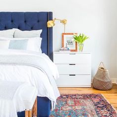 a bedroom with a blue headboard and white linens on the bed, along with a rug