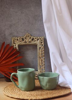 two green cups sitting on top of a rug next to a framed photo and red plant