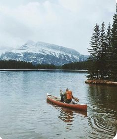 a man in a canoe on a lake with mountains in the background