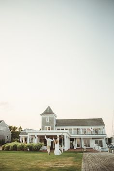 a bride and groom standing in front of a large white house on the ocean shore