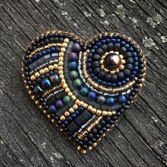 a heart shaped beaded brooch sitting on top of a piece of wooden plank