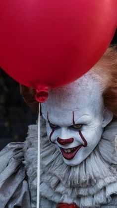 a creepy clown holding a red balloon