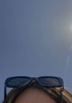 the sun shines brightly through sunglasses on top of a woman's head in front of a clear blue sky