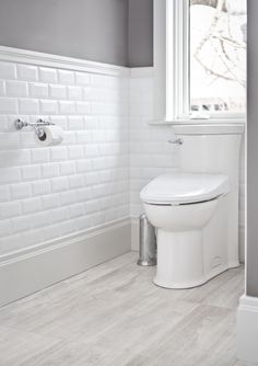 a white toilet sitting next to a window in a bathroom on top of a hard wood floor