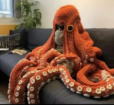 an orange octopus blanket sitting on top of a couch next to a stuffed animal in it's mouth