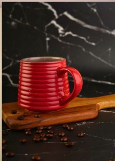 a red coffee mug sitting on top of a wooden cutting board next to coffee beans