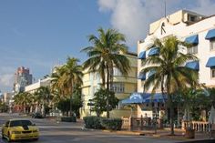 a yellow car is driving down the street in front of some buildings and palm trees