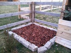 a garden bed made out of bricks and wood chips in a fenced backyard area