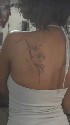 the back of a woman's white dress with a flower tattoo on her left shoulder