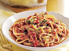 a white bowl filled with pasta and meat on top of a yellow place mat next to silverware