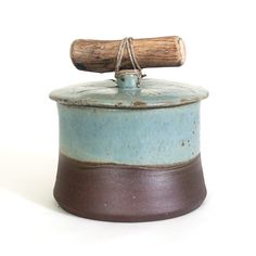 a blue and brown ceramic container with a wooden handle on it's top, against a white background