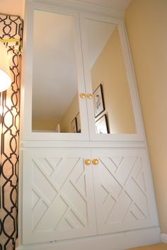 a white cabinet sitting next to a wall with a mirror on it's side