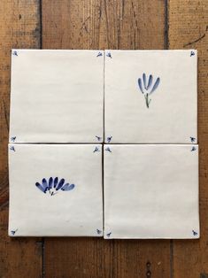 four white tiles with blue designs on them sitting on a wooden floor, one is square and the other is rectangle