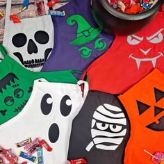 various halloween shirts and candy are on the floor next to a bowl full of candies