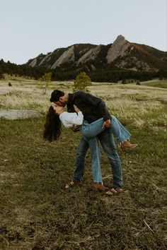 a man and woman kissing in the middle of a field with mountains in the background