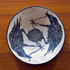 a bowl with two birds on it sitting on top of a wooden table next to a wall