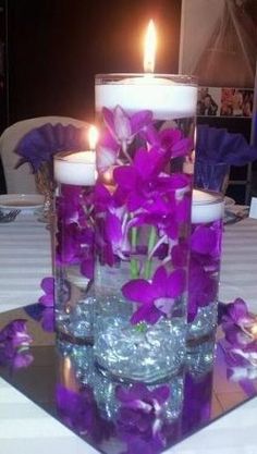 two candles are sitting on a table with purple flowers