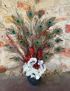 a vase filled with flowers and peacock feathers on top of a stone floor next to a brick wall