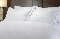 a bed with white sheets and pillows in a hotel room at the foot of a night stand