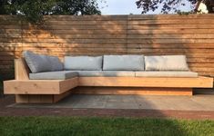 a couch sitting on top of a wooden bench in front of a wooden wall and grass