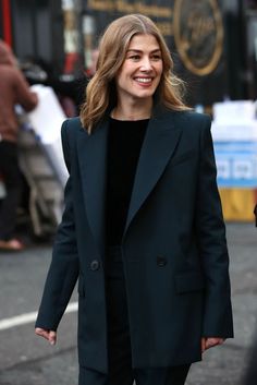 a woman is walking down the street wearing a black coat and pants, smiling at the camera