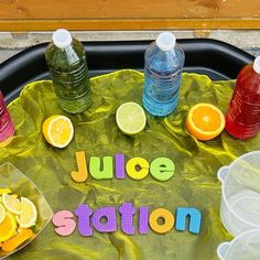 a tray that has some water, oranges and lemons on it with the word juice station spelled out