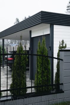 a car is parked in front of a house with a black fence and trees behind it