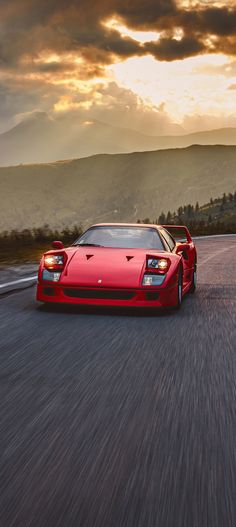 a red sports car driving down the road in front of a mountain range at sunset