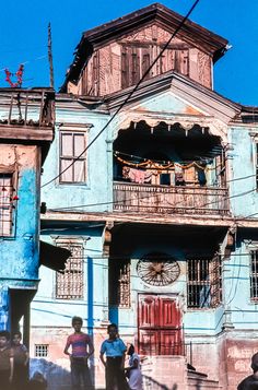 people are standing in front of an old blue building with a clock on the side