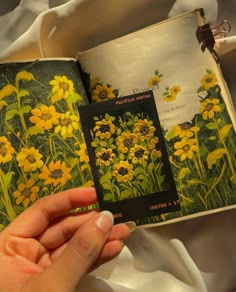 a hand holding an open book with yellow flowers