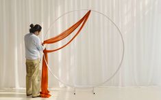 a woman standing in front of a white curtain with an orange ribbon around her neck