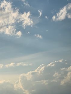 the airplane is flying high in the sky with clouds behind it and blue skies above