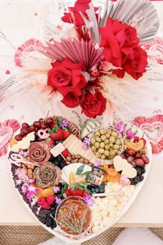 a heart shaped platter filled with lots of food and flowers on top of a table