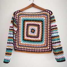 a crocheted sweater hanging on a wooden hanger